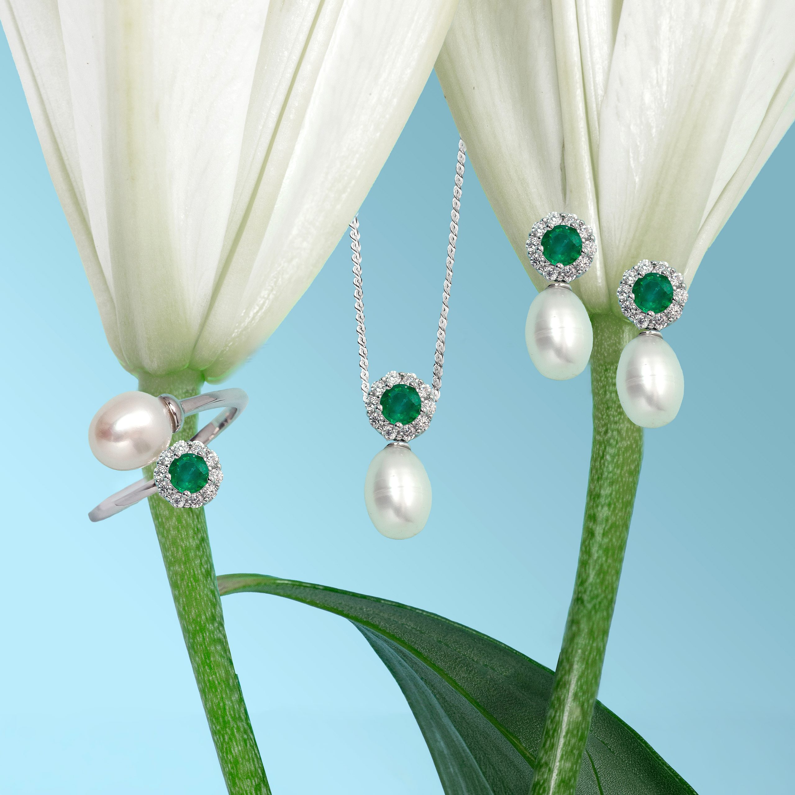 _NZR1342 Emerald and diamond jewelry hanging from plant stems against a blue gradient background.